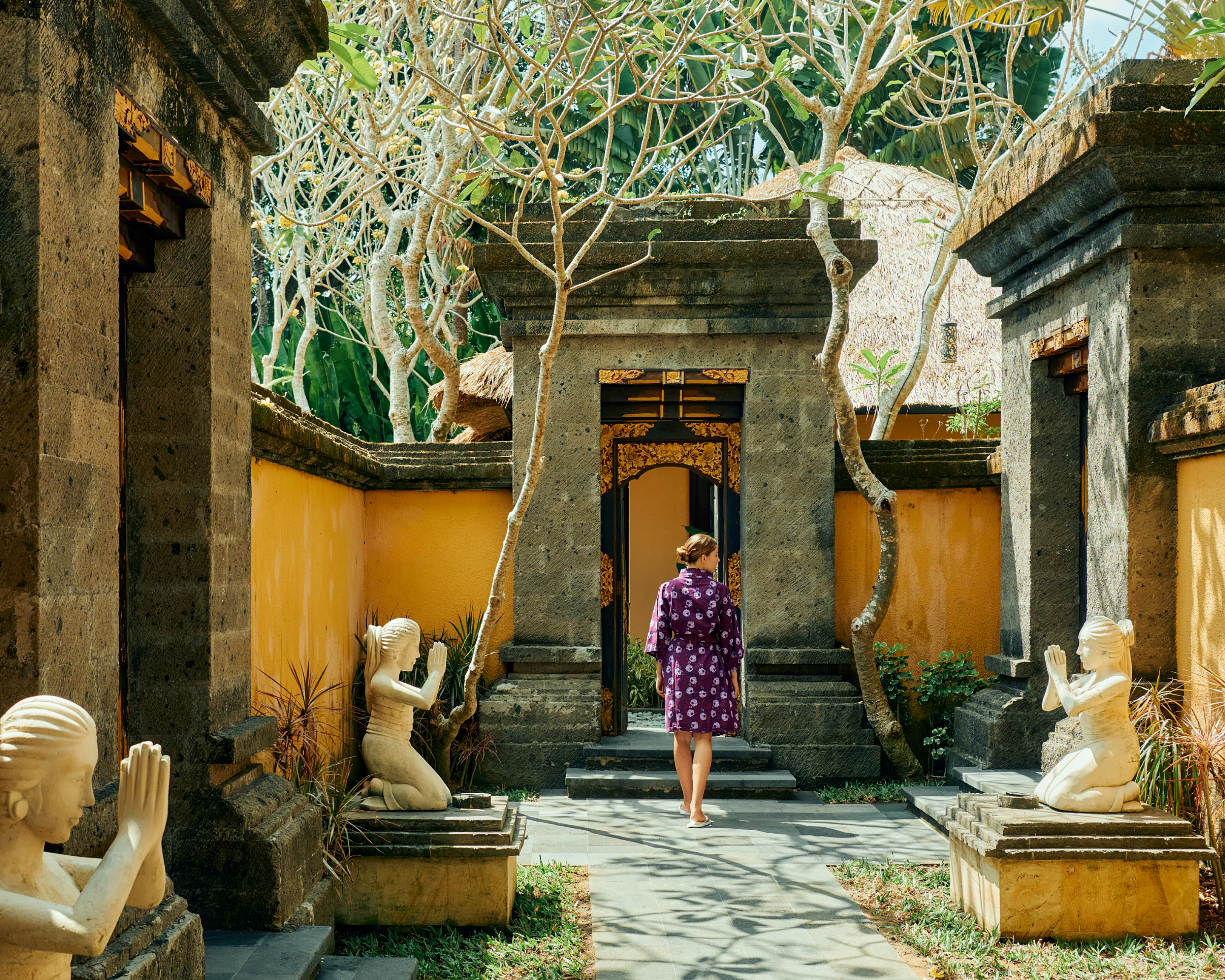 Woman in a purple robe walking through a Balinese temple door